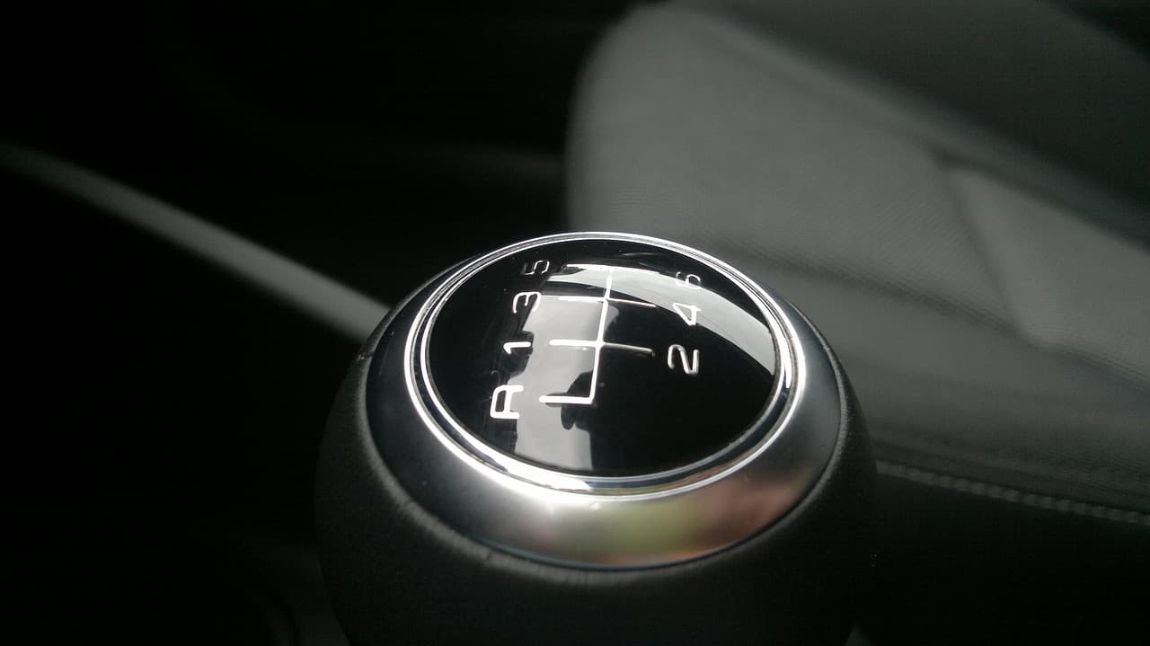The top of a manual gear knob in a dark car interior, its shift pattern engraved in the chrome