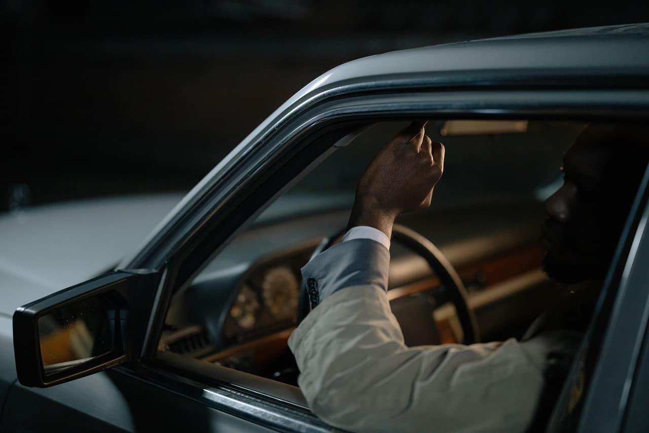 A driver's hand resting on the wheel of a car, seen through the open window