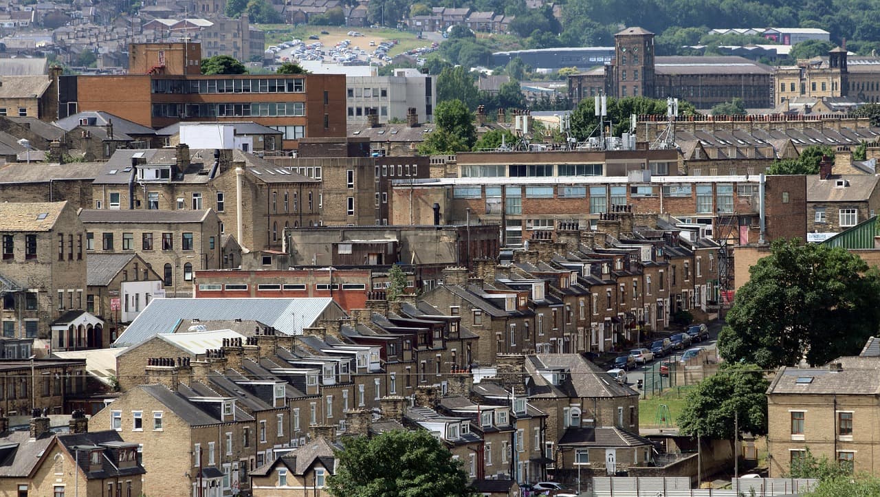 Rows of stone terraced houses climbing a northern English hillside, with a town centre beyond